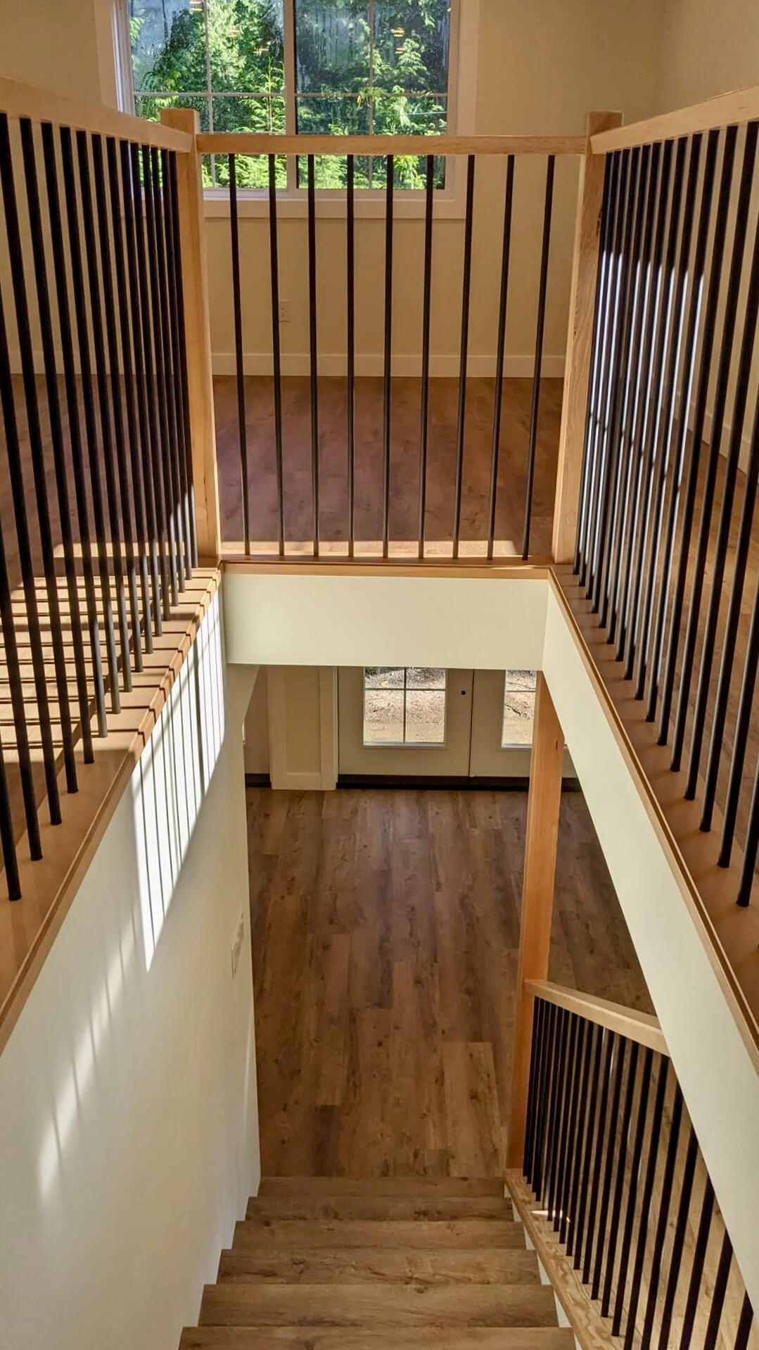 Open-Concept Upper Landing & Modern Staircase View looking down a wooden staircase with black metal spindles and modern luxury vinyl plank flooring