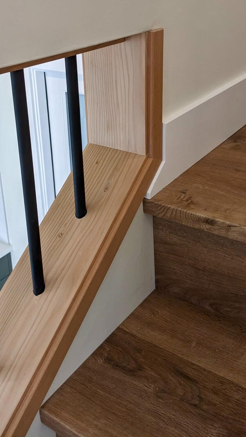 Custom Handrail & Wood Trim Craftsmanship Close-up detail of custom light wood handrail joinery and black metal spindle mounting.