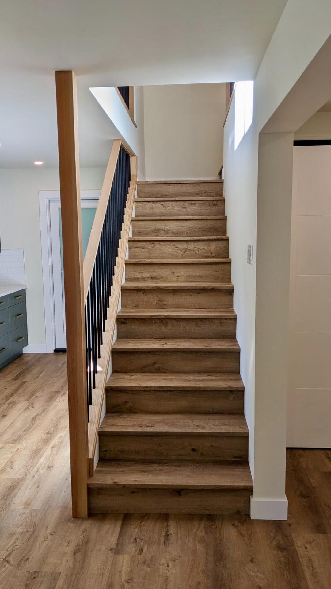 Interior straight staircase with natural wood treads, white risers, and black iron balusters.